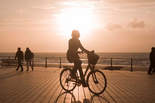 a silhouette of woman on a bicycle while in the rays of the setting sun on the embankment by the north sea in oostende. High quality photo