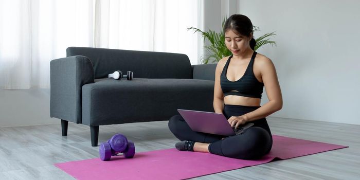 Woman using laptop while exercising at home. Female in sportswear sitting on floor and watching exercise video for her workout..