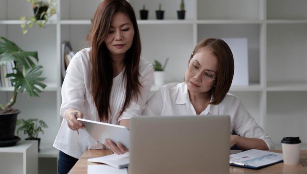 Two women analyzing documents while sitting on a table in office. Woman executives at work in office discussing some paperwork..