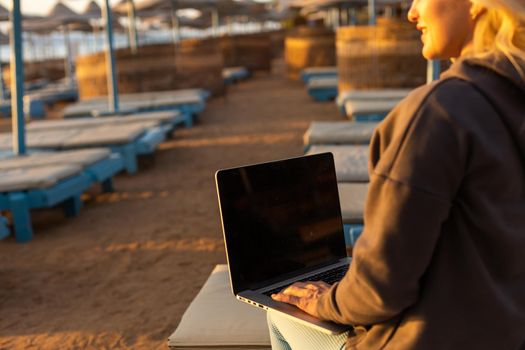 Woman sitting with laptop on the summer beach at sunset