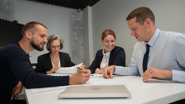 Four colleagues are discussing blueprints in a conference room in an office. Brainstorming of engineers and architects