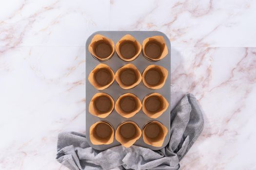Flat lay. Scooping dough into the cupcake pan lined with parchment muffin liners to bake sharlotka muffins.