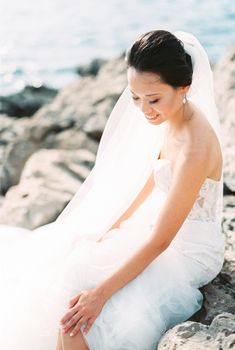 Smiling bride sitting on stones with her hand on her knee. High quality photo