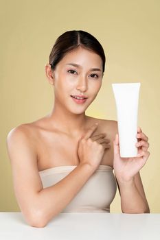 Ardent woman smiling holding mockup product for advertising text place, light grey background. Concept of healthcare for skin, beauty care product for advertising.
