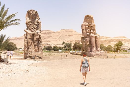 Female tourist walking towards the ancient egyptian statues of the Pharaoh Amenophis. Colossi of Memnon.