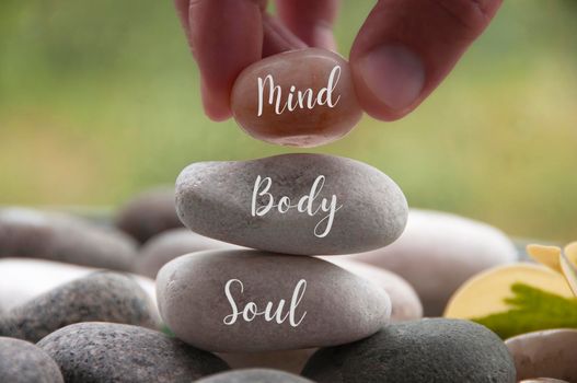 Hand holding zen stone with words Mind, Body, Soul. Spa concept.