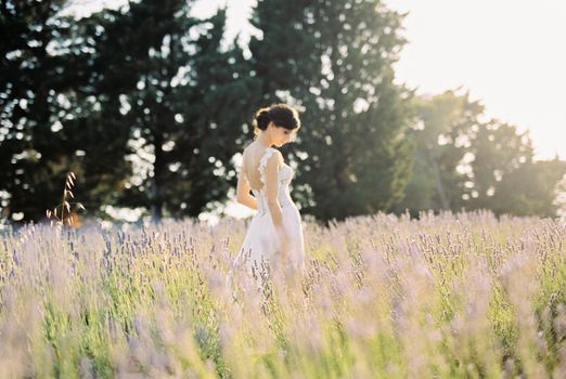 Bride in a white dress stands in a lavender field with her head down. Side view. High quality photo