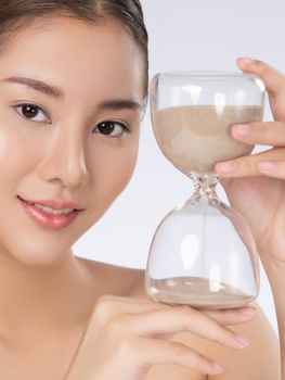 The concept of anti-aging demonstrated by a closeup portrait of gorgeous young woman holding an hourglass. Skincare treatment, beauty care.