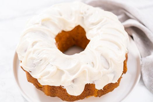 Freshly baked pumpkin bunt cake with cream cheese frosting on the kitchen counter.