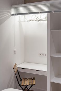 White study table combined with wardrobe with wooden shelves and a chair in a small student room for rent