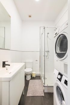 Small and narrow white bathroom with shower cabin, washing machine and dryer.