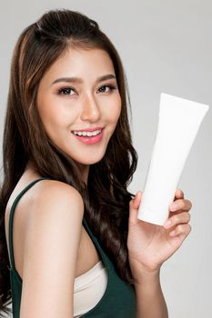 Closeup ardent woman smiling holding mockup product for advertising text place, light grey background. Concept of healthcare for skin, beauty care product for advertising.