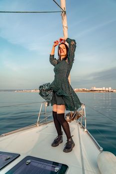 Woman standing on the nose of the yacht at a sunny summer day, breeze developing hair, beautiful sea on background.