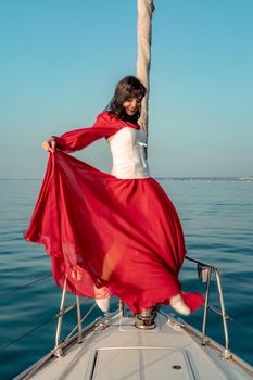 Attractive middle-aged woman in a red dress on a yacht on a summer day. Luxury summer adventure, outdoor activities