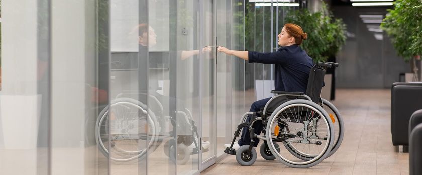 Red-haired caucasian woman in a wheelchair trying to open the door in the office