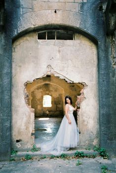 Bride stands near the dilapidated entrance of the old fortress. High quality photo