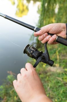 Fishing Reel. The guy spins the coil on the background of the lake. The concept of relaxation and hobby for the soul