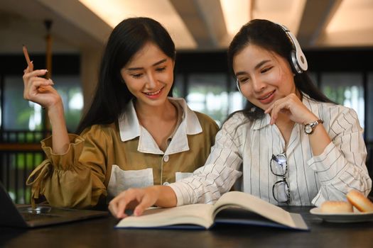 Concentrated asian students preparing for exams, learning together in college library. Education, people and technology concept.