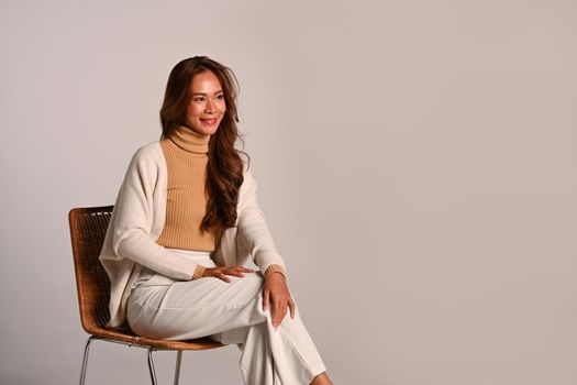 Gorgeous woman wearing stylish trendy clothes in earth tones sitting on beige background. Autumn and Winter concept.