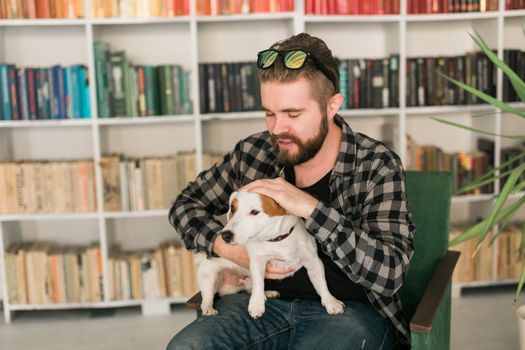 Happy male owner of jack russell terrier dog, feels responsibility of caring about pet, standing against bookshelves background. People and relationship with animals.