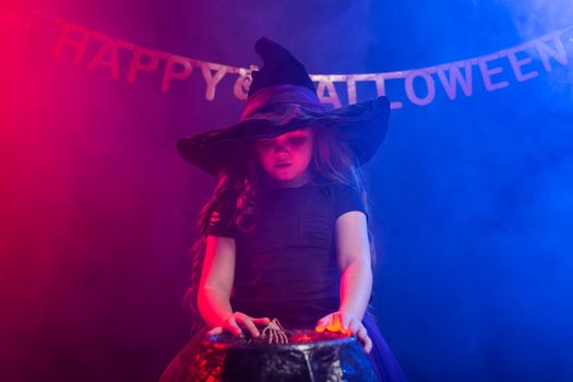 Little witch child cooking potion in the cauldron on Halloween