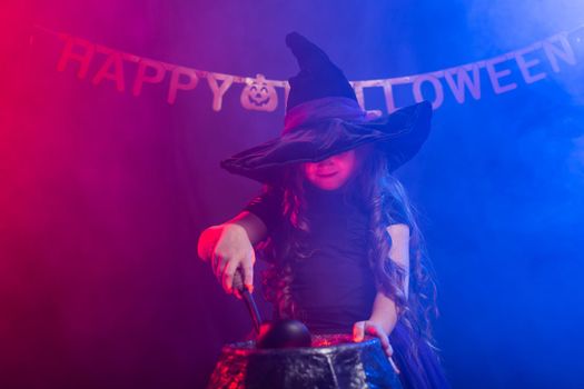 Little witch child cooking potion in the cauldron on Halloween