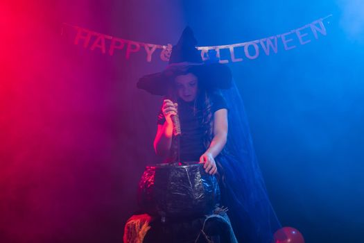 Child girl witch preparing a potion in the cauldron at halloween holidays