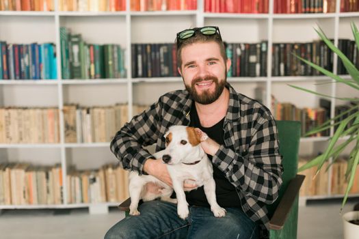 Happy male owner of jack russell terrier dog, feels responsibility of caring about pet, standing against bookshelves background. People and relationship with animals.