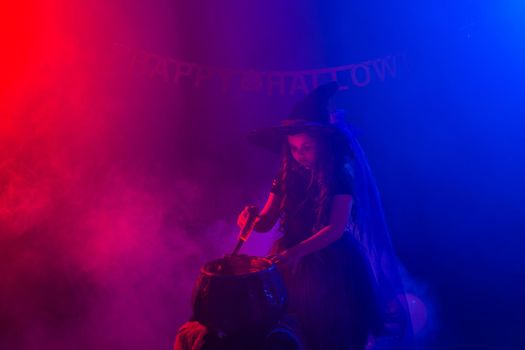 Little witch child cooking potion in the cauldron on Halloween