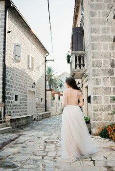 Bride in a white dress walks along a narrow street of an old town. Back view. High quality photo