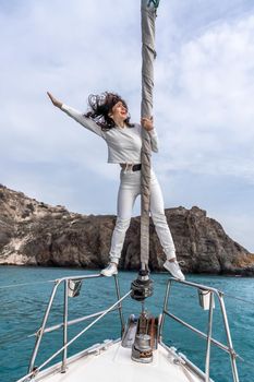 Woman standing on the nose of the yacht at a sunny summer day, breeze developing hair, beautiful sea on background.