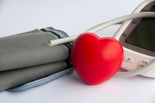 Digital blood pressure monitor and heart shape on white background.