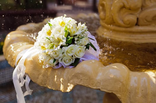 The Wedding Bouquet Of The Bride Of Red Roses Lies In An Old Fountain Under Splashes And Drops Of Water.. bridal bouquet of flowers in fountain water drops