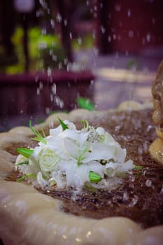 The Wedding Bouquet Of The Bride Of Red Roses Lies In An Old Fountain Under Splashes And Drops Of Water.. bridal bouquet of flowers in fountain water drops