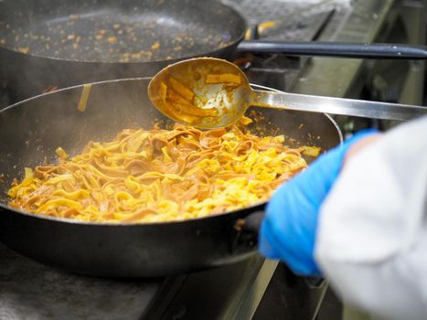 mixing pasta with sauce in a big professional used professional pan