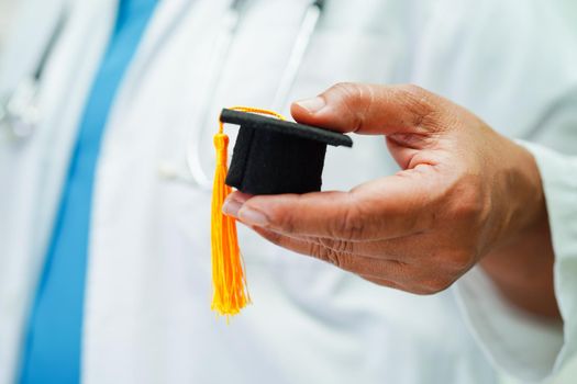 Asian woman doctor holding graduation hat in hospital, Medical education concept.