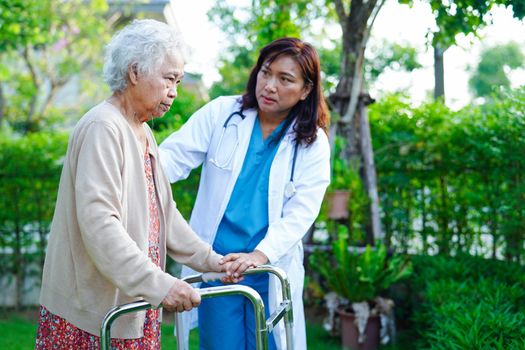 Doctor help Asian elderly woman disability patient walk with walker in park, medical concept.