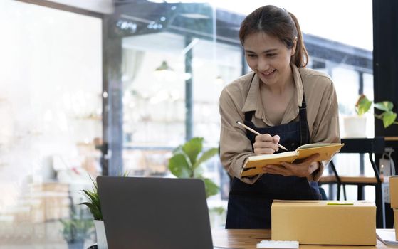 Young smiling beautiful owner asian woman freelancer sme business online shopping working on laptop computer with parcel box at home - SME business online and delivery concept.