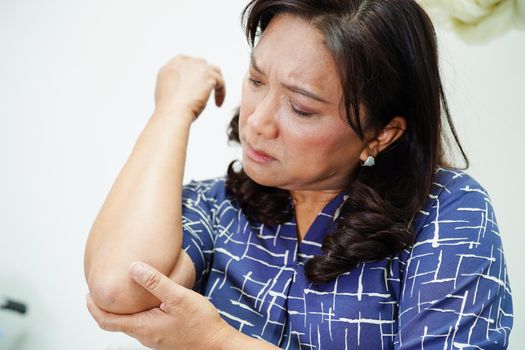 Asian senior woman wearing elastic support elbow brace for reduce pain.