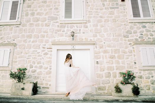 Bride holds the hem of her long lace dress near the old stone house. High quality photo