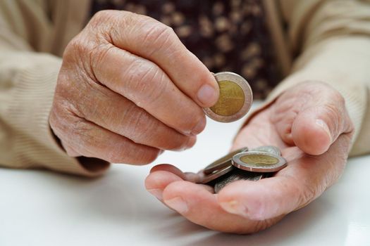 Retired elderly woman counting coins money and worry about monthly expenses and treatment fee payment.