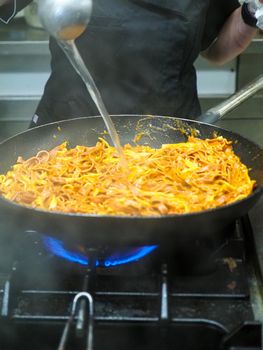 mixing pasta with sauce in a big professional used professional pan
