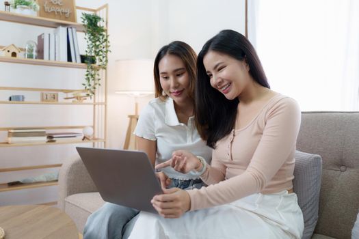 Two asian women having nice lively conversation in living room on sofa in cozy interior.