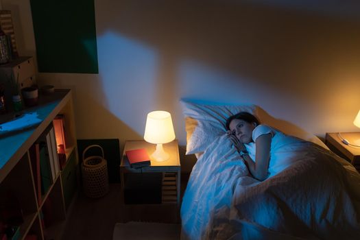 Beautiful girl suffering from insomnia lying in her bed with Blue Colors from the moon. High quality photo