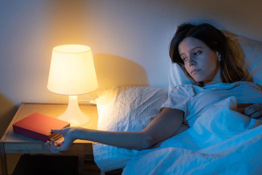 Beautiful girl suffering from insomnia getting a book to read in the middle of the night. Night activity. High quality photo