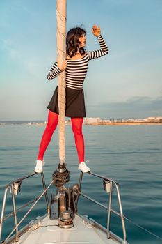 Woman standing on the nose of the yacht at a sunny summer day, breeze developing hair, beautiful sea on background.