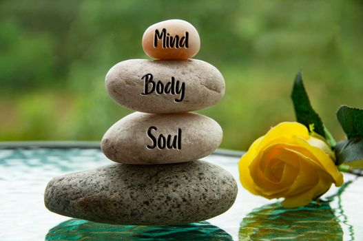 Mind, Body and Soul words engraved on zen stones with blurred nature and yellow rose background. Copy space and zen concept.