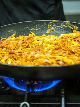 mixing pasta with sauce in a big professional used professional pan