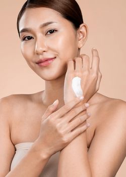 Closeup ardent girl with soft makeup looking at camera, applying moisturizing skincare cream on her hand, isolated background. Skincare cream applied by female model concept.