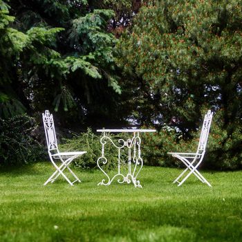 White garden furniture on the lawn. A chair and a table in the garden. Equipped backyard.